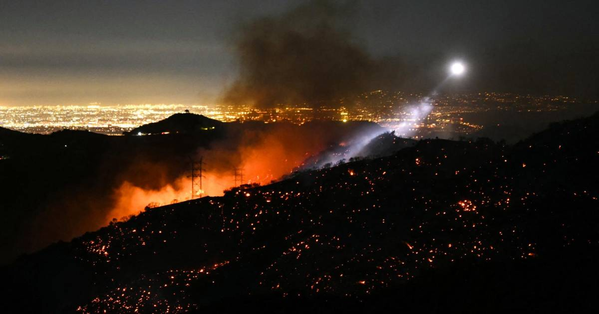 Incendio nocturno en la ladera de una colina con una ciudad iluminada al fondo.