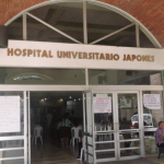 Entrada principal de un hospital con personas sentadas afuera.