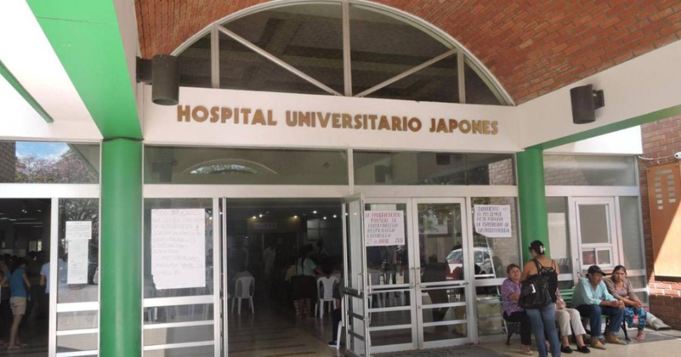 Entrada principal de un hospital con personas sentadas afuera.