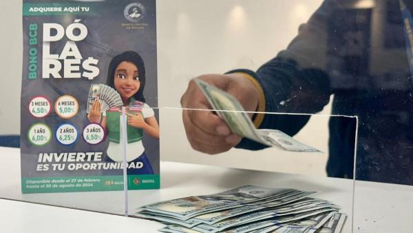 Persona depositando billetes en una caja transparente junto a un cartel promocional.
