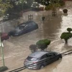 Inundación en una calle con coches parcialmente sumergidos y árboles.