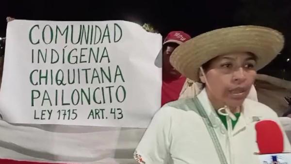 Persona con sombrero hablando frente a una pancarta que dice 'Comunidad Indígena Chiquitana Pailoncito Ley 1715 Art. 43'.