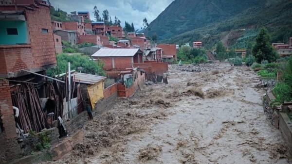 Río caudaloso pasando junto a casas de ladrillo, en un área montañosa.