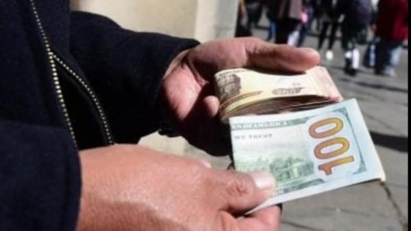 Persona sosteniendo un billete de 100 dólares y otros billetes.