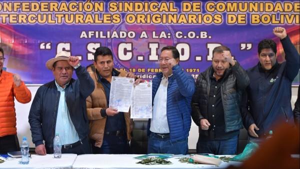 Un grupo de personas en una mesa levantando el puño, con un cartel detrás.