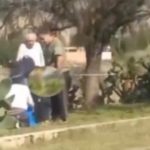 Una escena al aire libre con varias personas interactuando cerca de un arbusto.