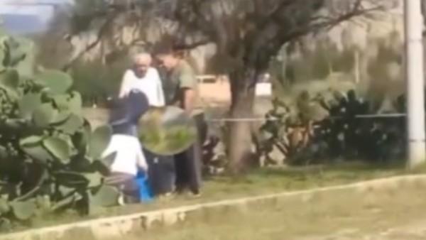 Una escena al aire libre con varias personas interactuando cerca de un arbusto.