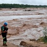 Rescatista de pie junto a un cauce de río crecido.