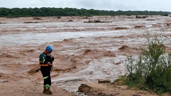 Rescatista de pie junto a un cauce de río crecido.