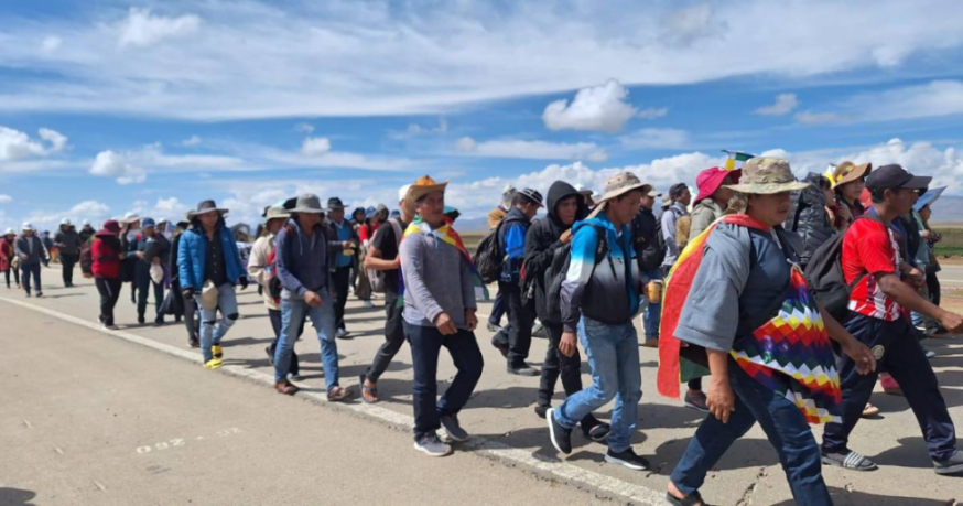Grupo de personas caminando por una carretera bajo un cielo azul con nubes.