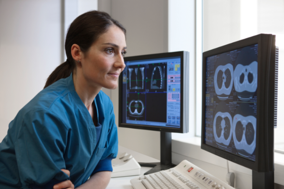 Una profesional de la salud observando imágenes médicas en dos monitores.