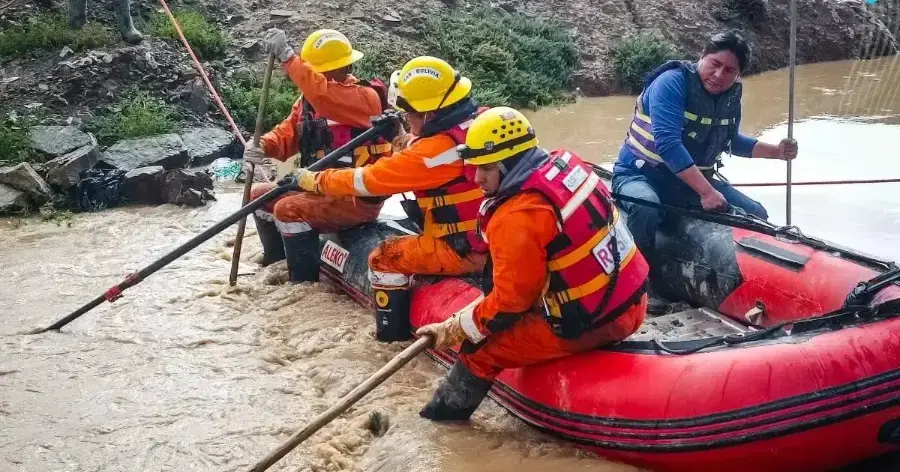 Unos rescatistas en un bote inflable en un río fangoso, con vegetación en el fondo.