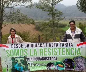 Dos personas sosteniendo una pancarta en un entorno rural.