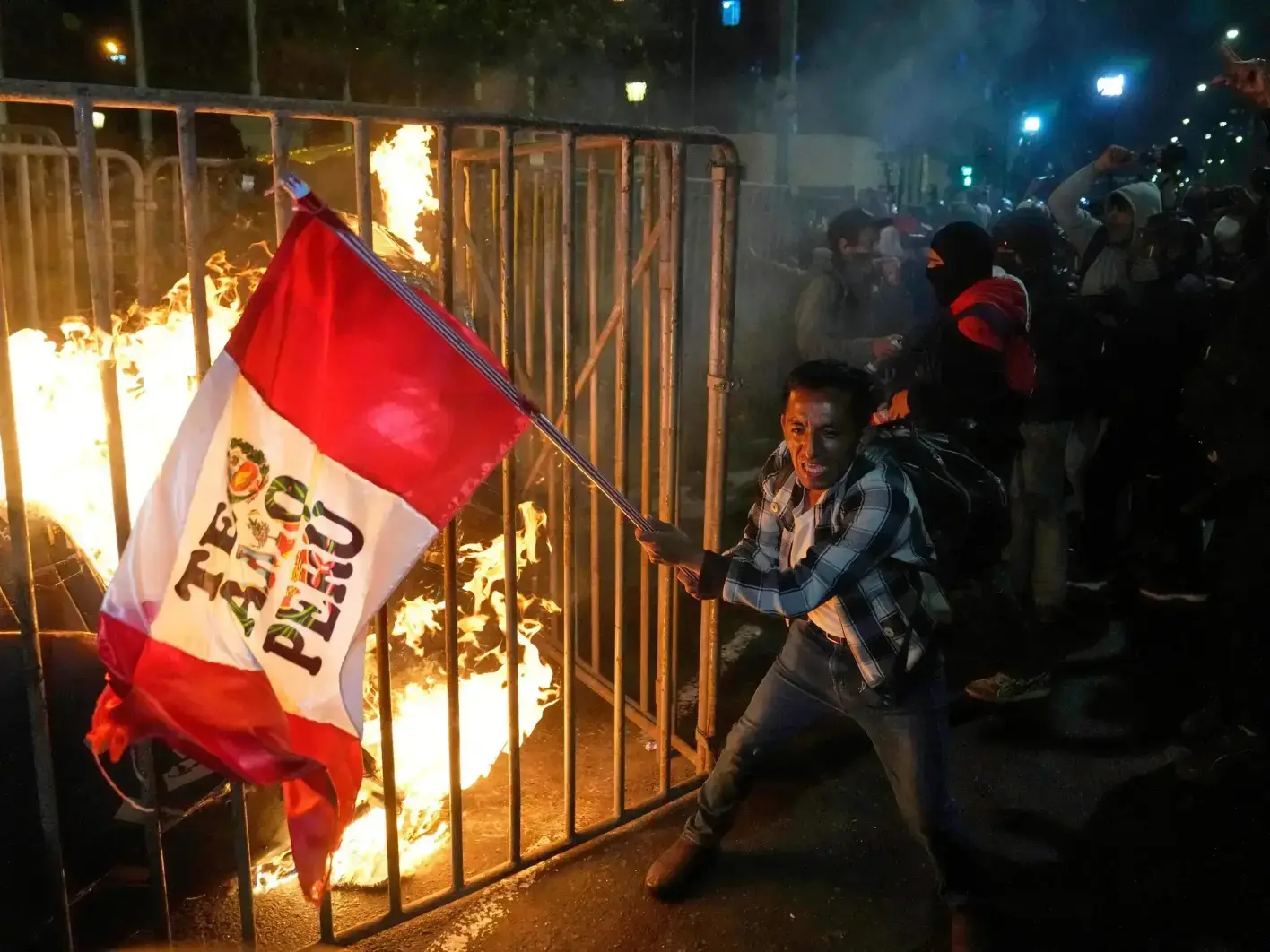 Un manifestante ondea una bandera peruana mientras un muñeco de cartón arde frente al Congreso.
