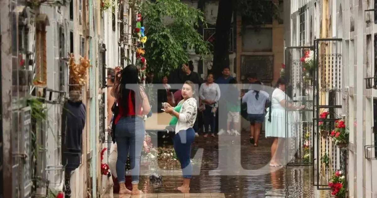 Personas se mojan por las precipitaciones mientras visitan el cementerio.