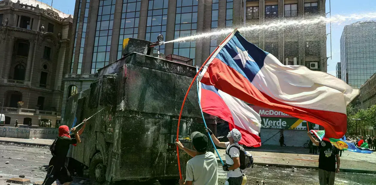 Manifestantes antigubernamentales se enfrentan a un cañón de agua de la policía cerca del Palacio de La Moneda en Santiago de