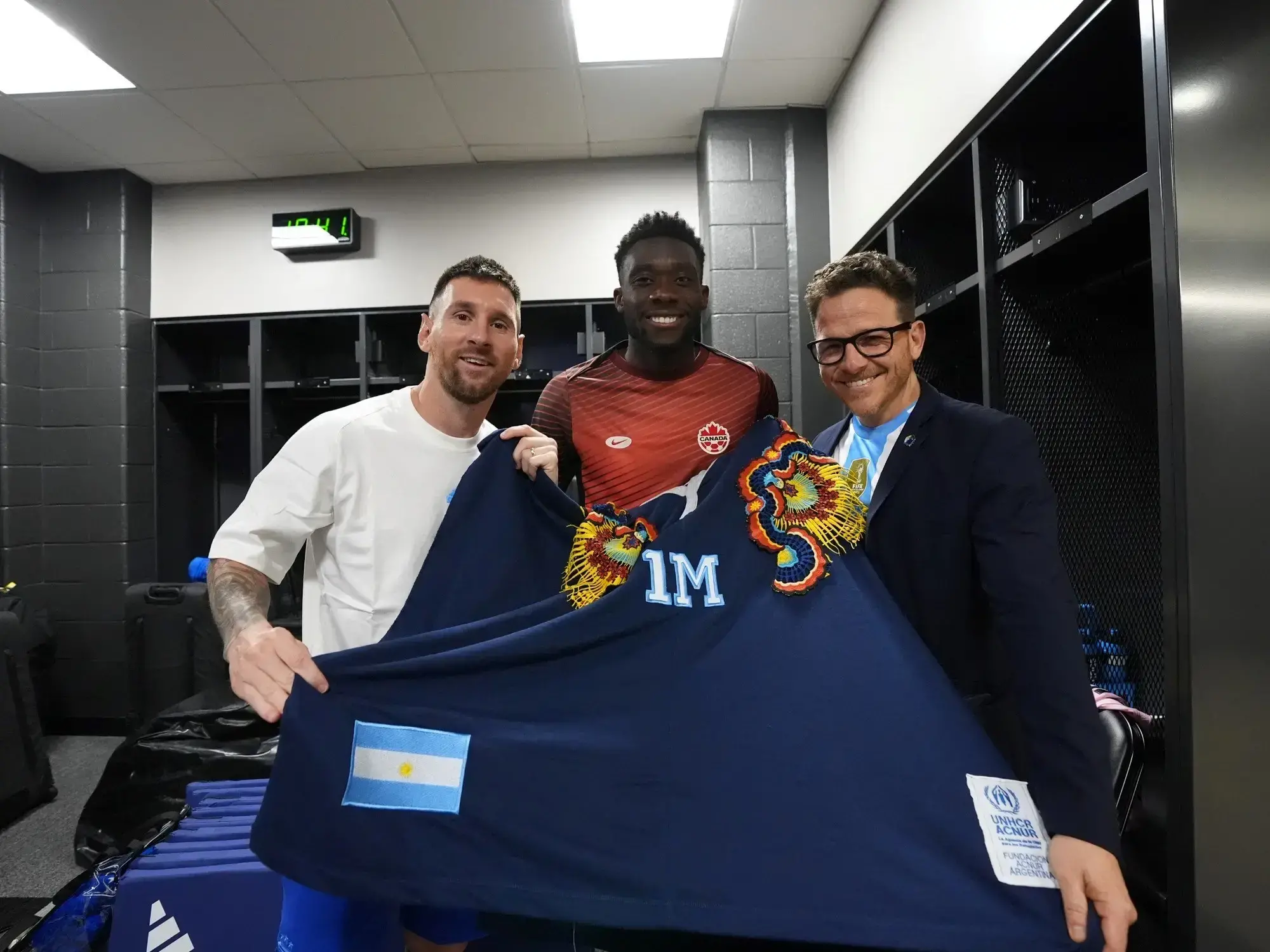 Lionel Messi y Alphonso Davis sostienen el poncho de la Fundación Acnur Argentina