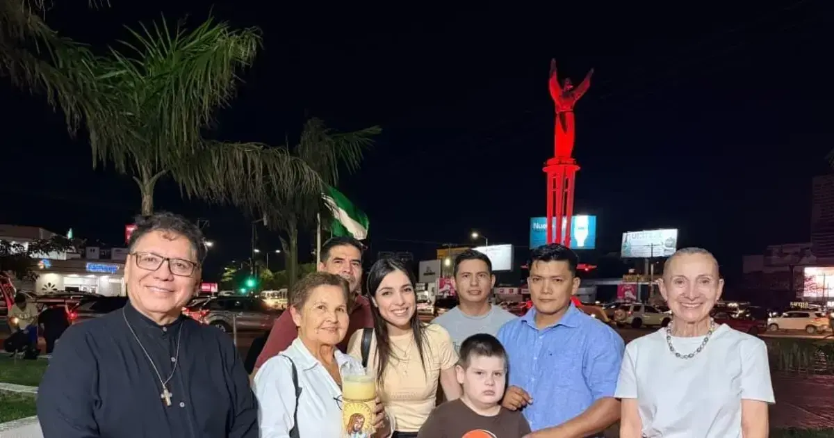 Autoridades eclesiales y municipales posan delante del Cristo Redentor iluminado de rojo