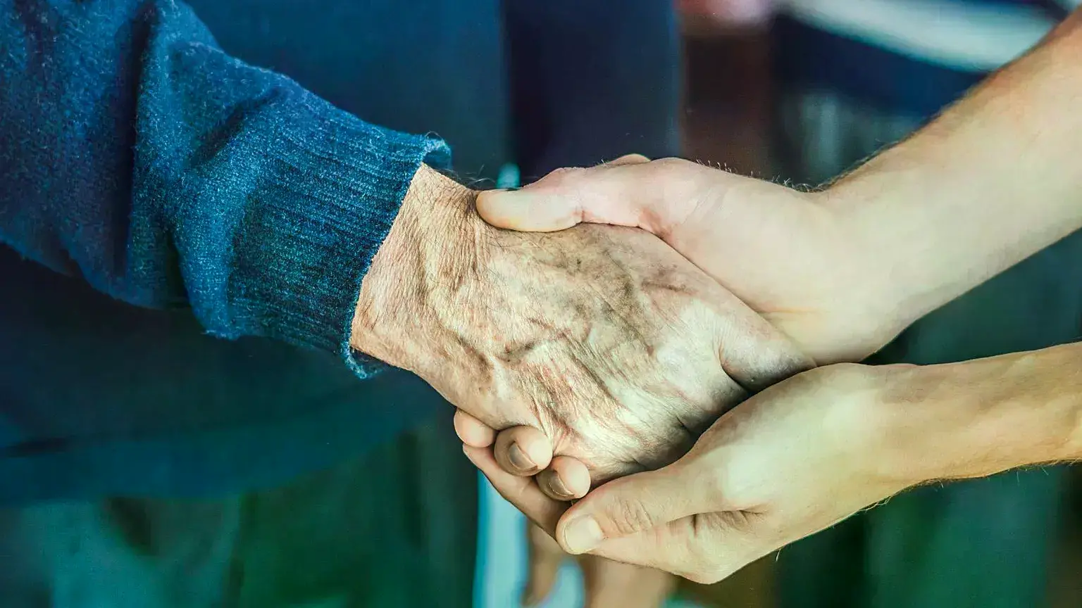 Una mujer sostiene la mano de una persona mayor.