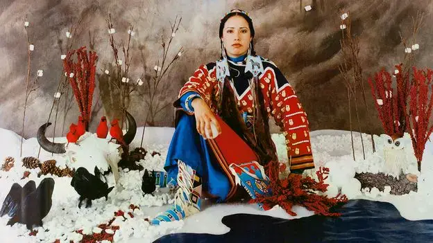 Wendy Red Star en su obra "Winter", rodeada de elementos artificiales que simulan un paisaje invernal.