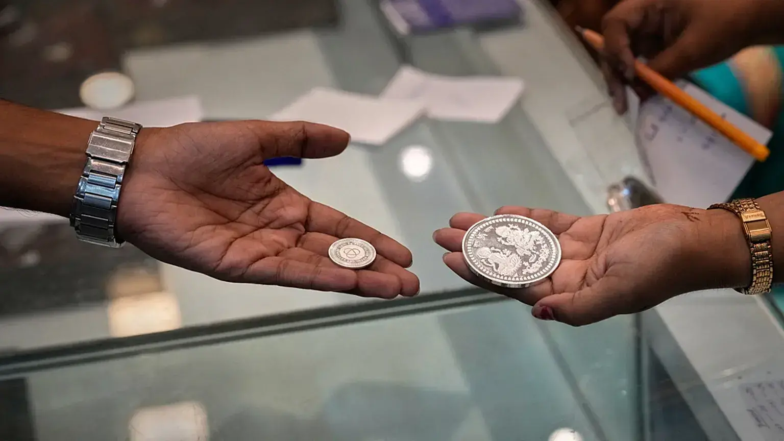 Una vendedora muestra una moneda de plata a un cliente durante Dhanteras, día propicio para comprar metales preciosos.