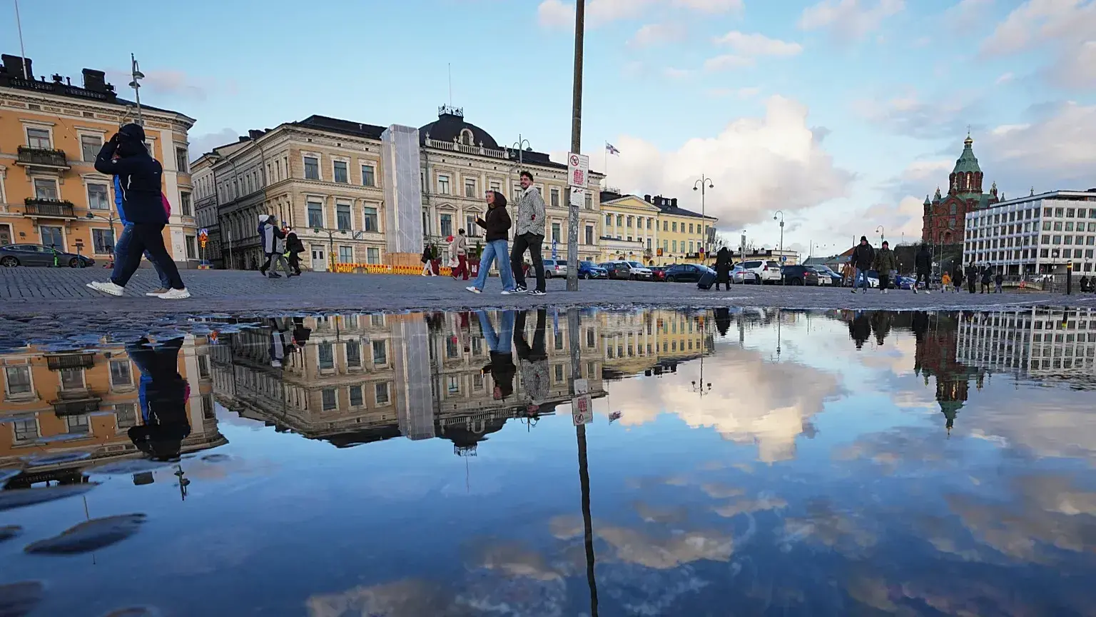 Personas caminan por una plaza reflejada en un charco en Helsinki, Finlandia.