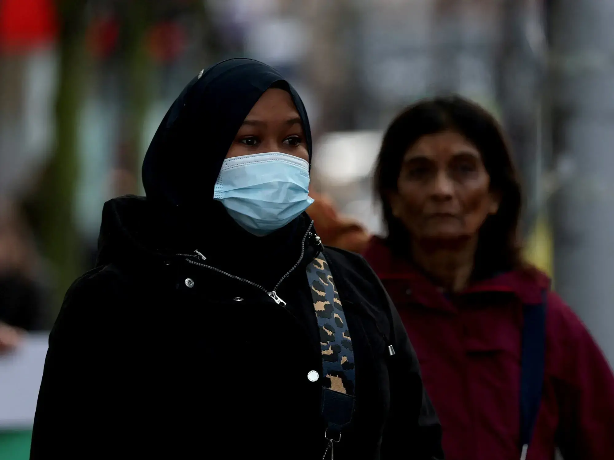 Una mujer con mascarilla espera en una parada de autobús, mientras aumentan las hospitalizaciones.