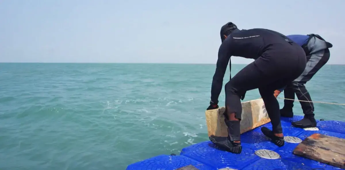 Miembros de Marine Conservation Cambodia cargan pilares de hormigón en una balsa.