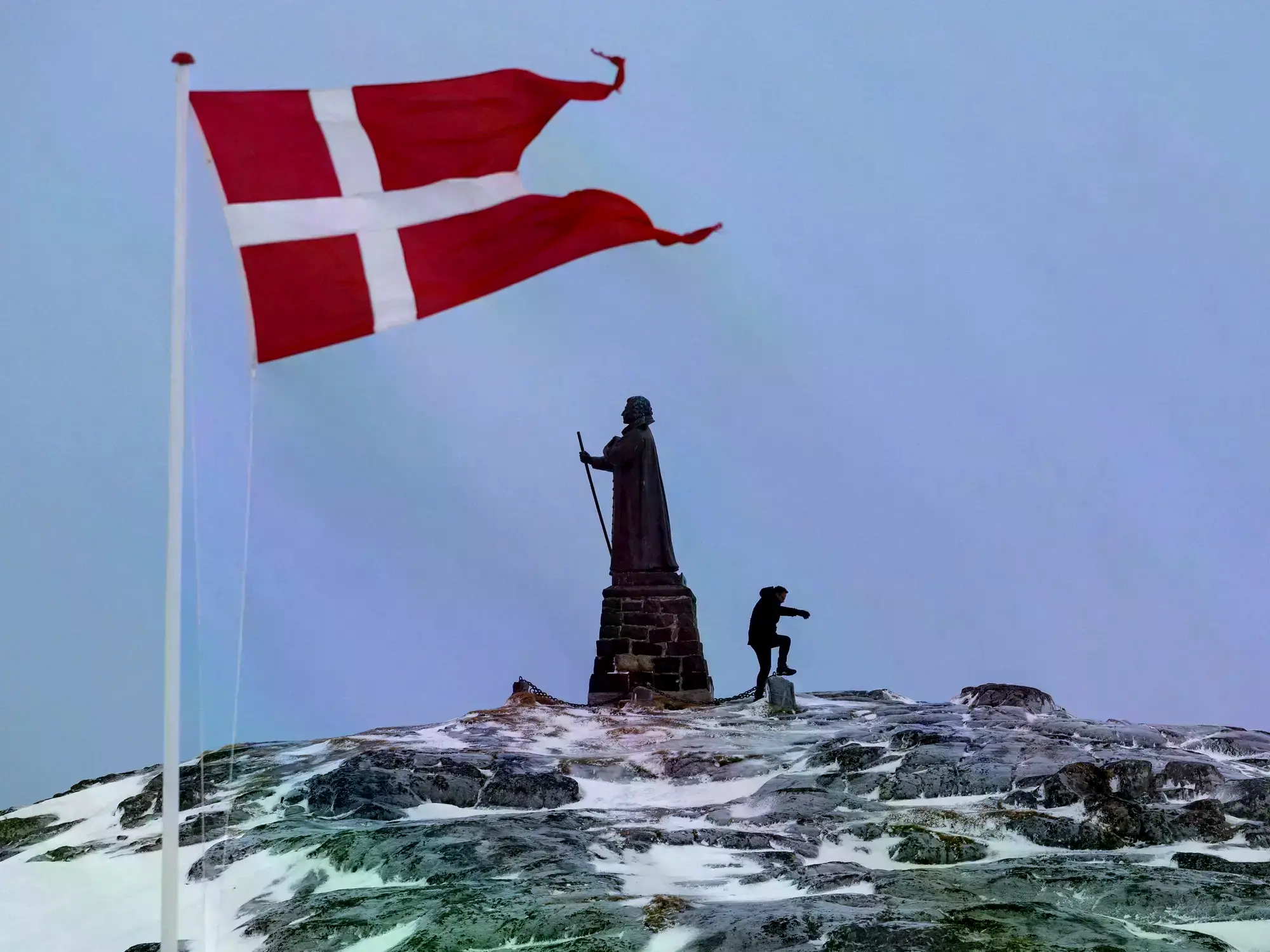 Un hombre camina mientras la bandera danesa ondea junto a la estatua de Hans Egede en Nuuk, Groenlandia.