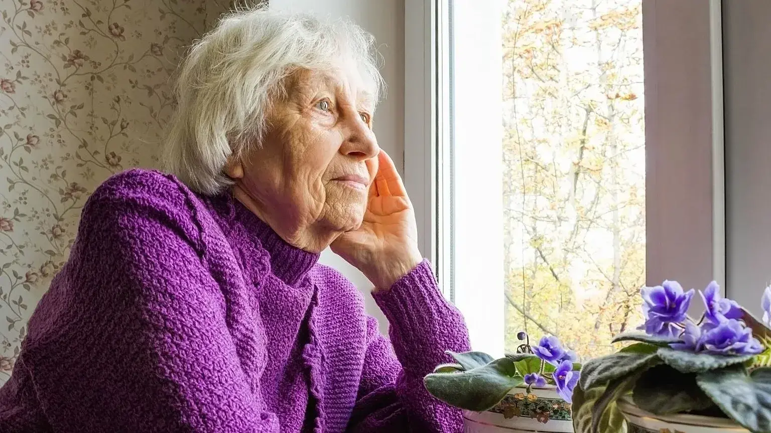Una mujer mayor mira por la ventana.