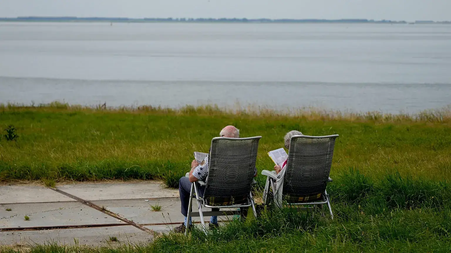 Una pareja de ancianos lee sentada frente a un río.