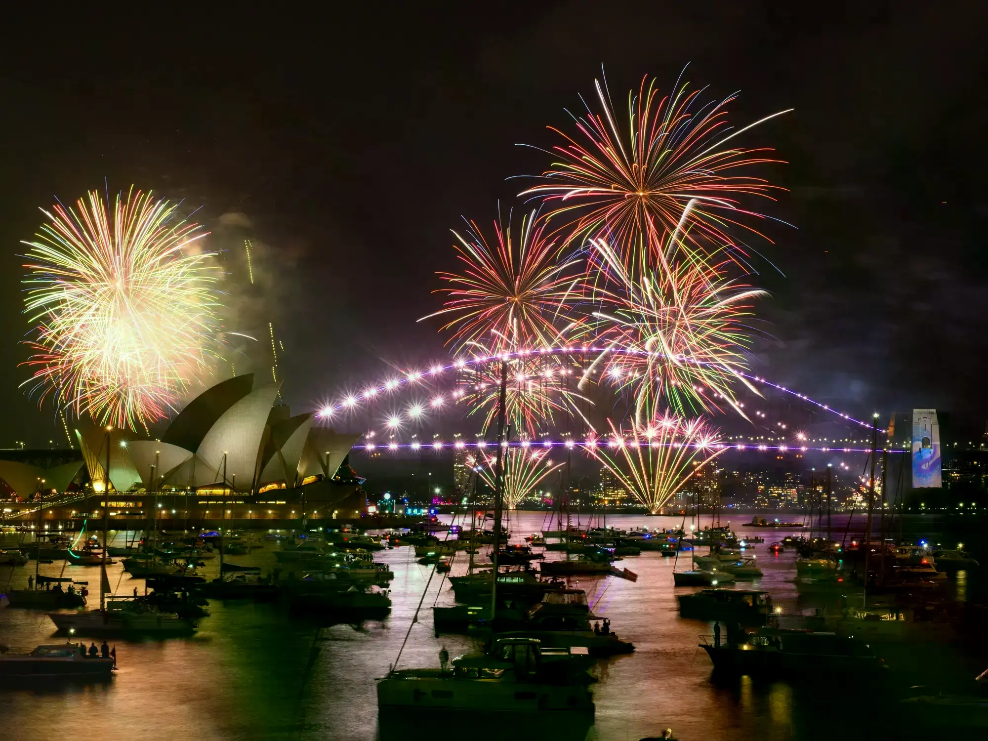 La gente enciende las linternas de sus teléfonos antes del espectáculo de fuegos artificiales de medianoche en Sídney.