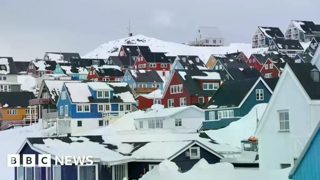Vista aérea de un asentamiento en Groenlandia con icebergs en el fondo.