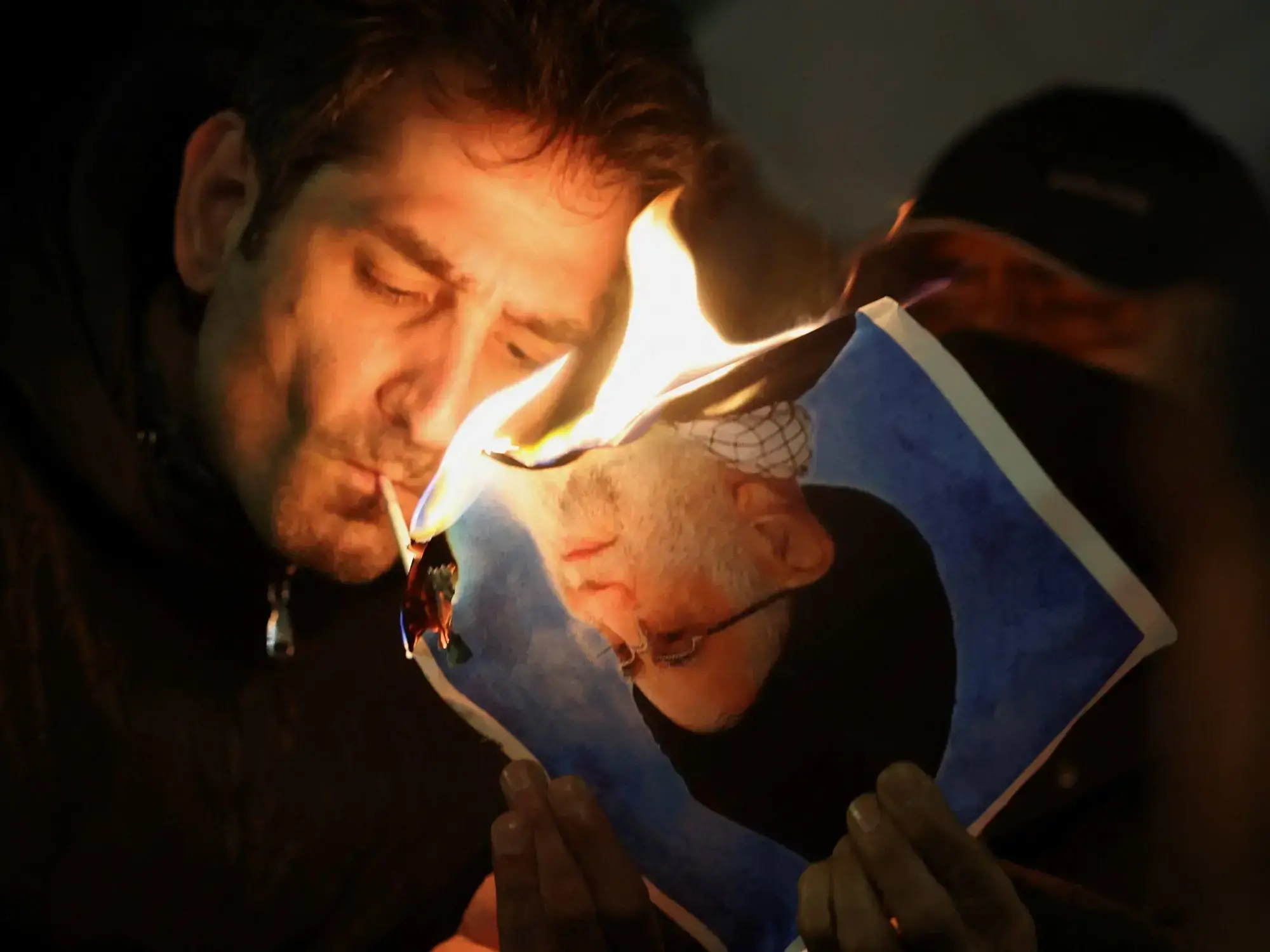 Un hombre enciende un cigarrillo con una foto quemada del líder supremo Ali Khamenei.