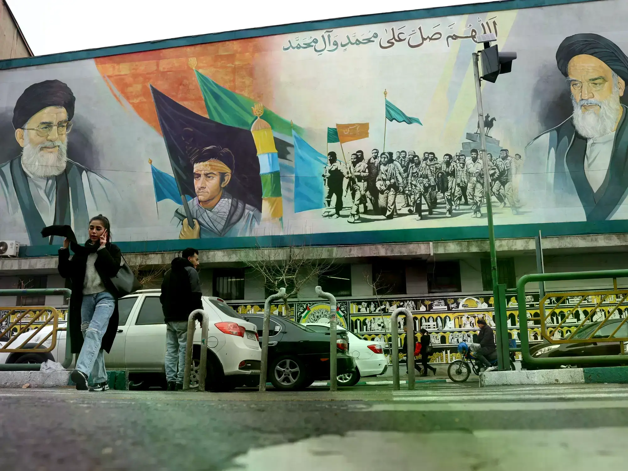 Iraníes caminan junto a un mural que muestra a Ali Jamenei y a Ruhollah Jomeini.