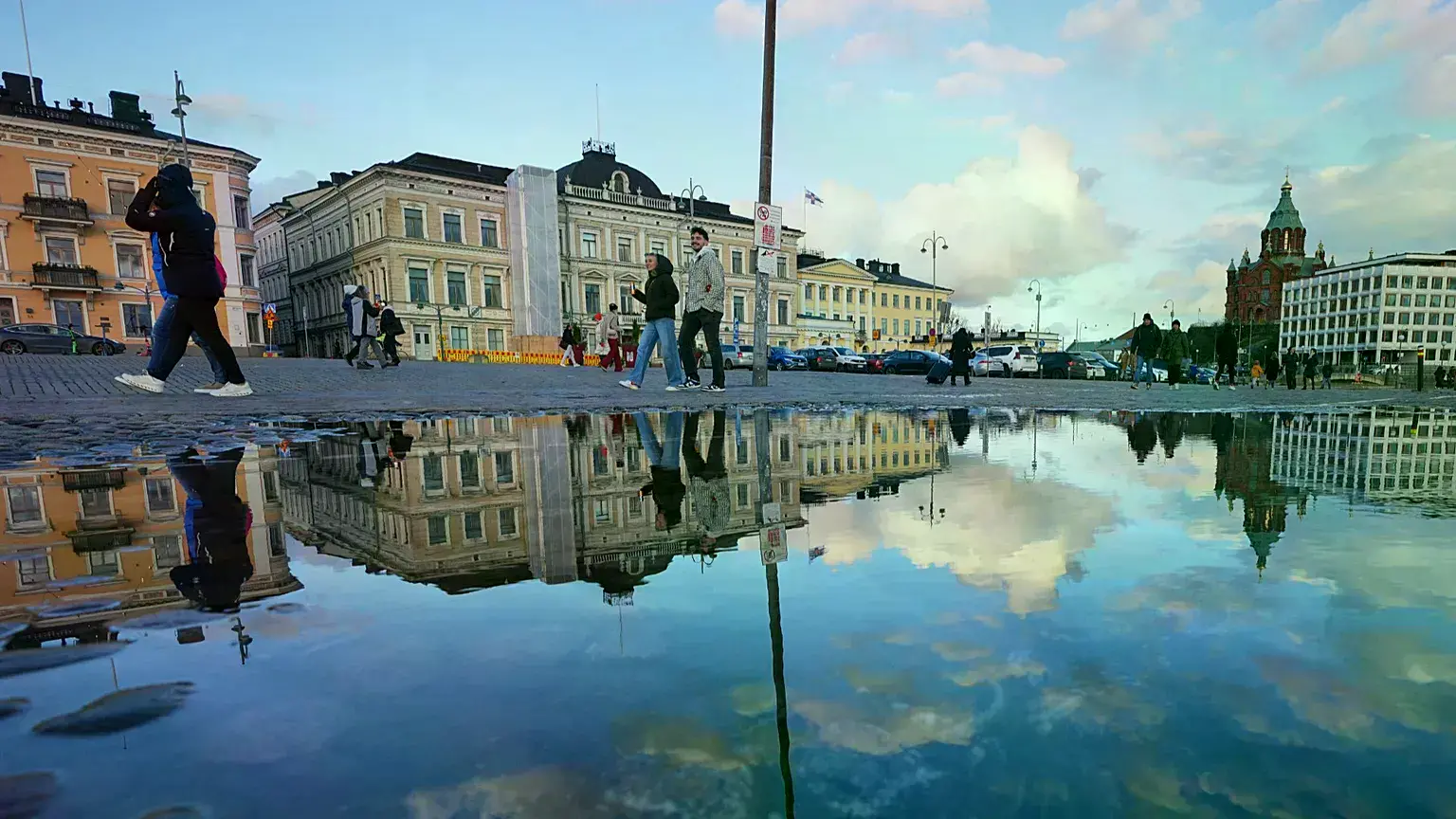 Personas caminan por una plaza reflejada en un charco en Helsinki, Finlandia.