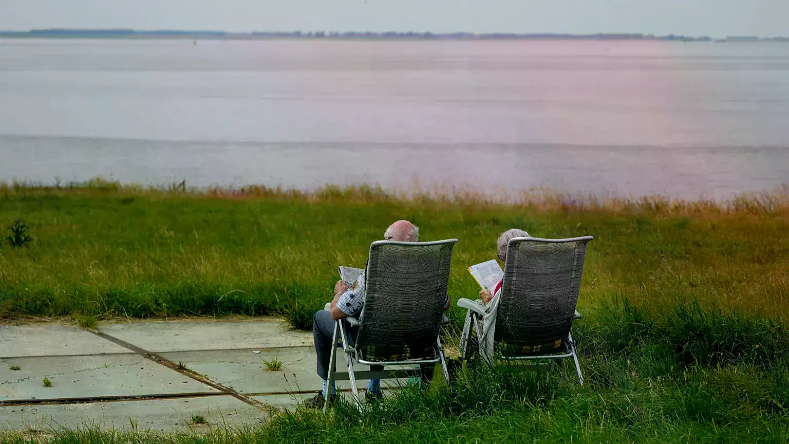 Una pareja de ancianos lee sentada frente a un río.