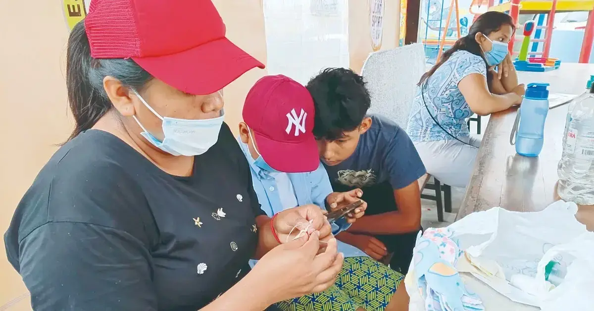 Thaner juega en el celular junto a un amigo, mientras su mamá aprovecha el momento para avanzar en su tejido.