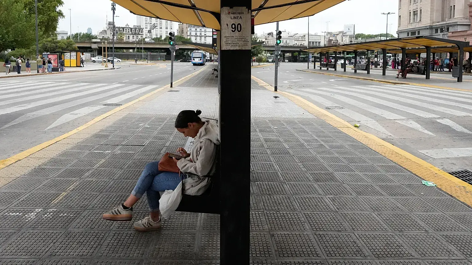 Una mujer sentada en una parada de autobús vacía debido a una huelga sindical.