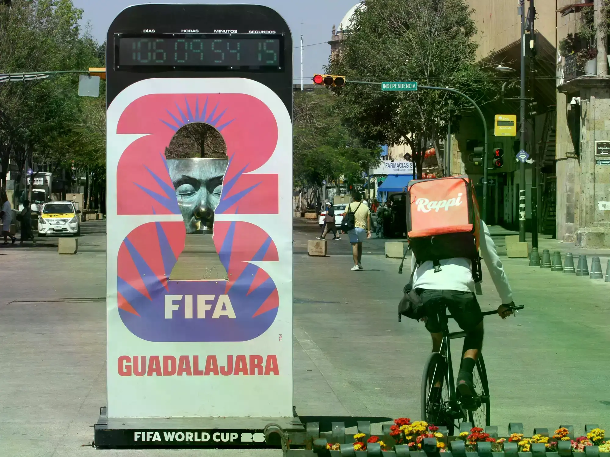Un repartidor de comida circula en bicicleta junto a un anuncio de la Copa Mundial de Fútbol FIFA 2026 en Guadalajara.