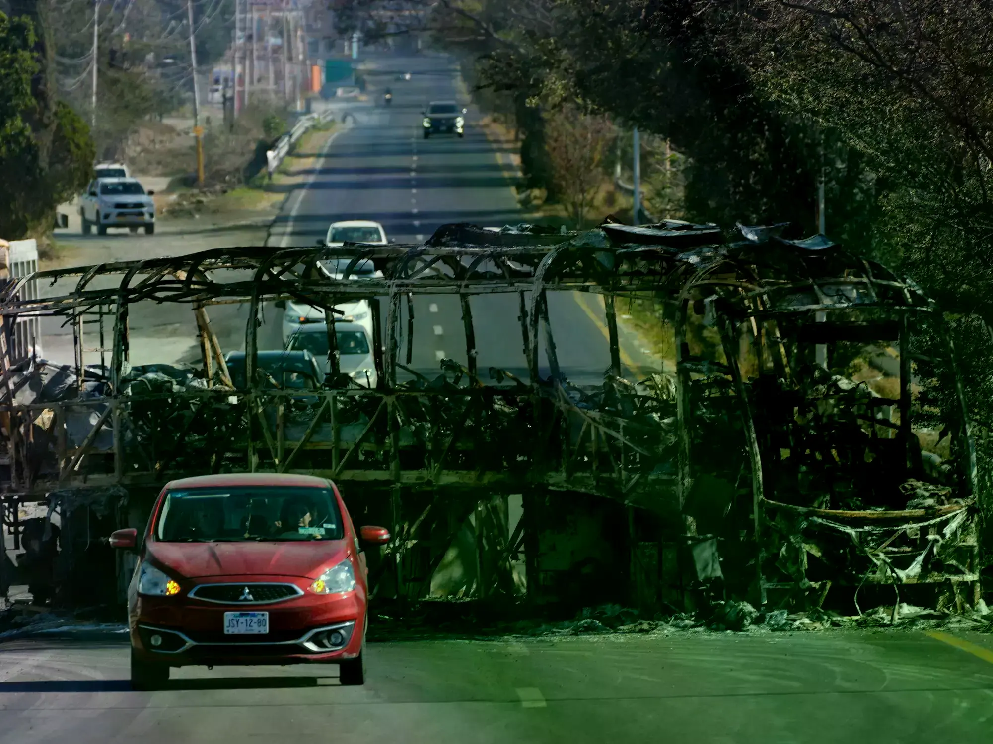 Un vehículo pasa junto a un autobús incendiado en Guadalajara.