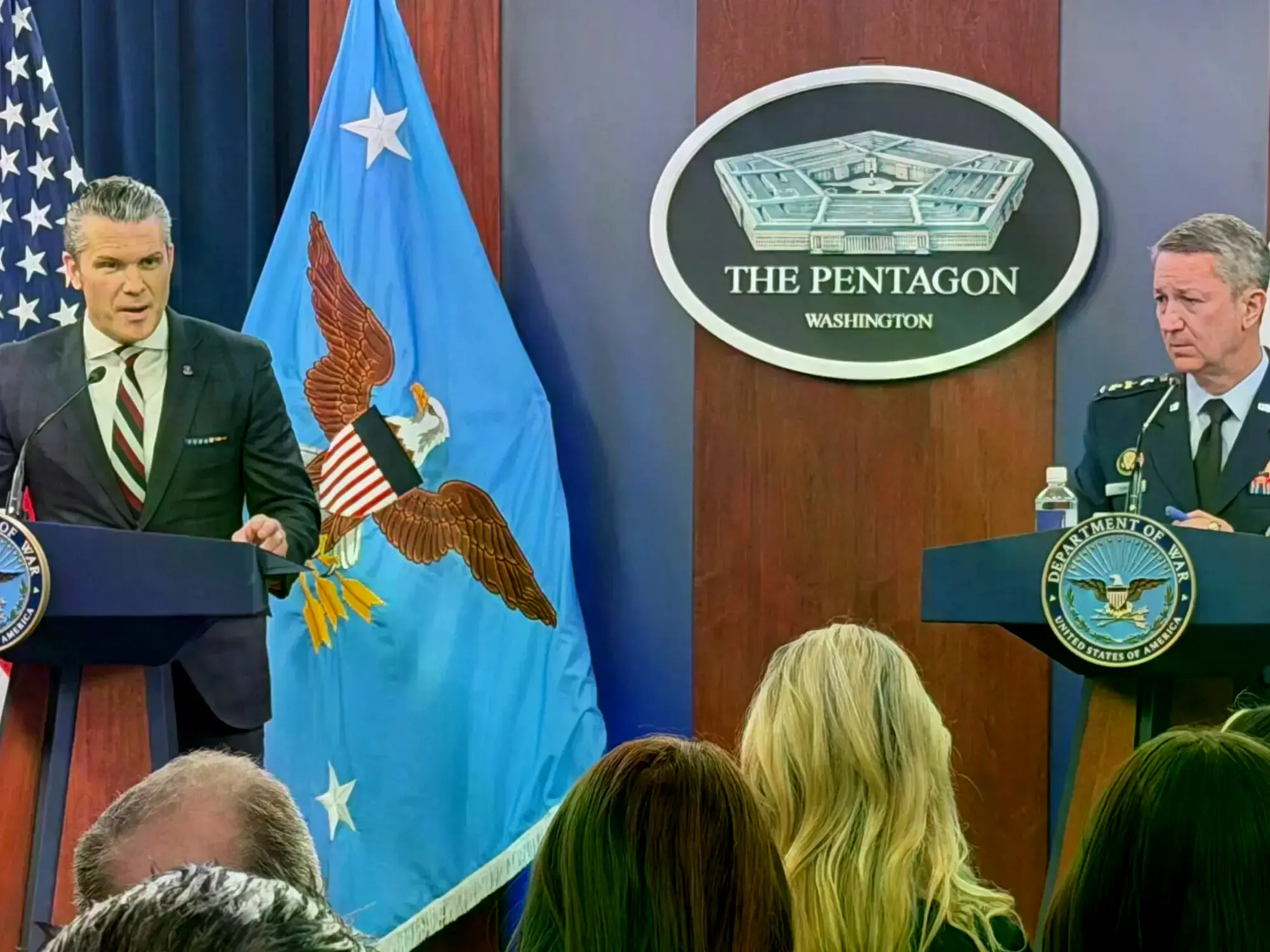 Pete Hegseth escucha al general Dan Caine en una rueda de prensa.