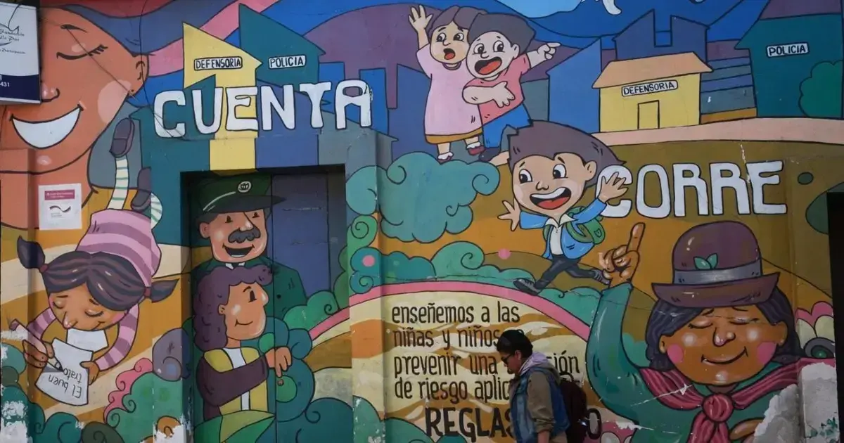 Una persona camina frente a un mural alusivo a la niñez en La Paz.