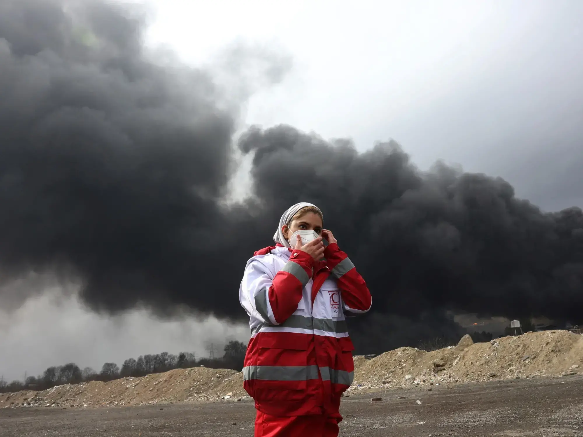 Una integrante de la Media Luna Roja de Irán se cubre del humo tras un ataque a una refinería en Teherán.