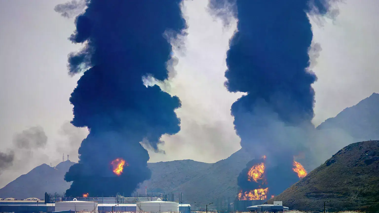 Columnas de humo y fuego se elevan después de que restos de un dron iraní interceptado alcanzaran una instalación petrolera e