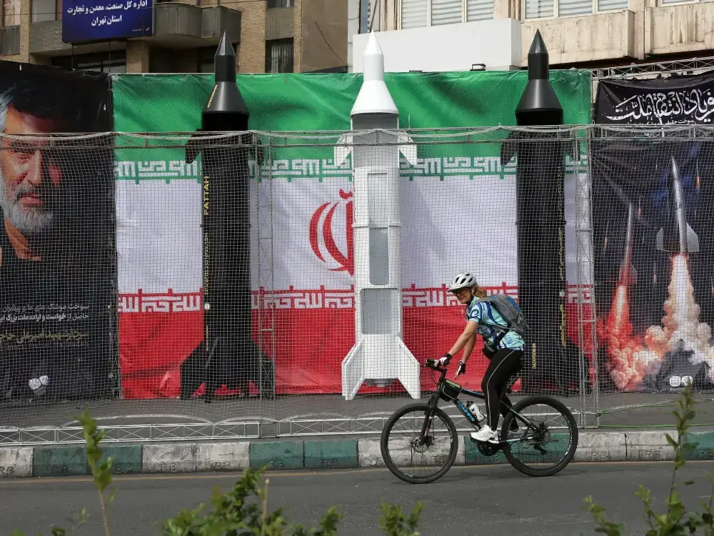 Un ciclista iraní pasa junto a propaganda del régimen en Teherán.