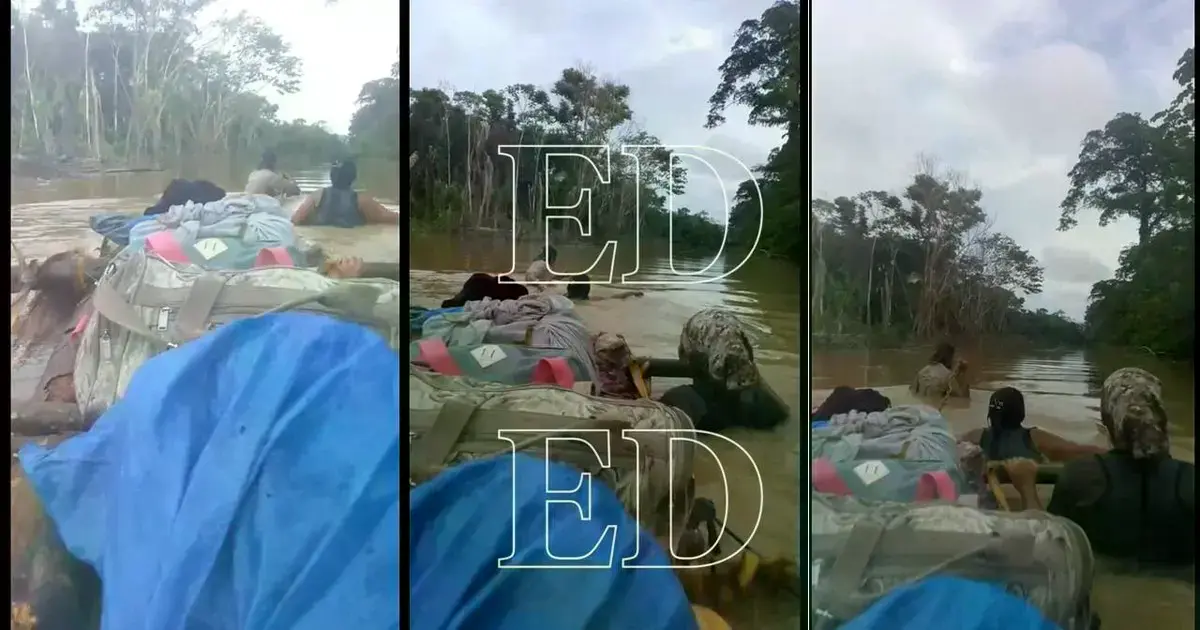 Personas empujan una canoa artesal cargada en medio de una calle inundada.