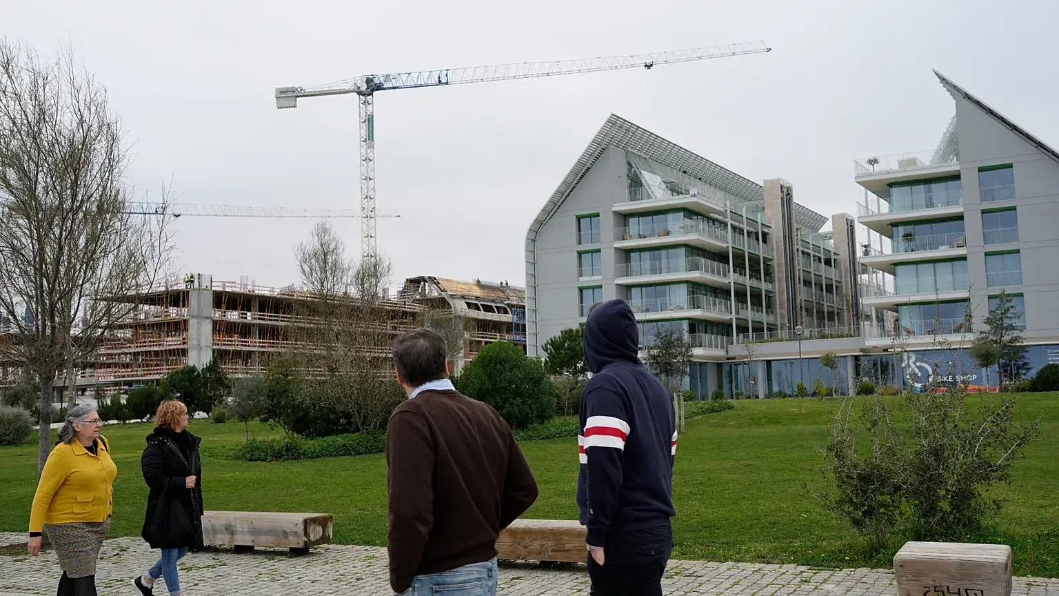 Personas que pasean junto al río Tajo observan nuevos edificios de lujo en Lisboa.