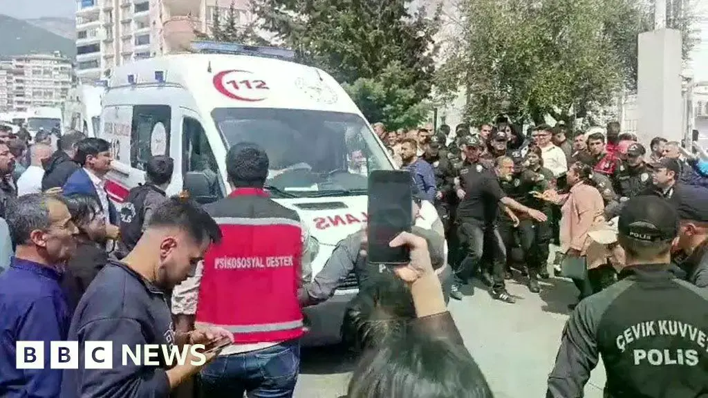 Ambulancias y furgonetas de policía fuera de la escuela, con padres angustiados.