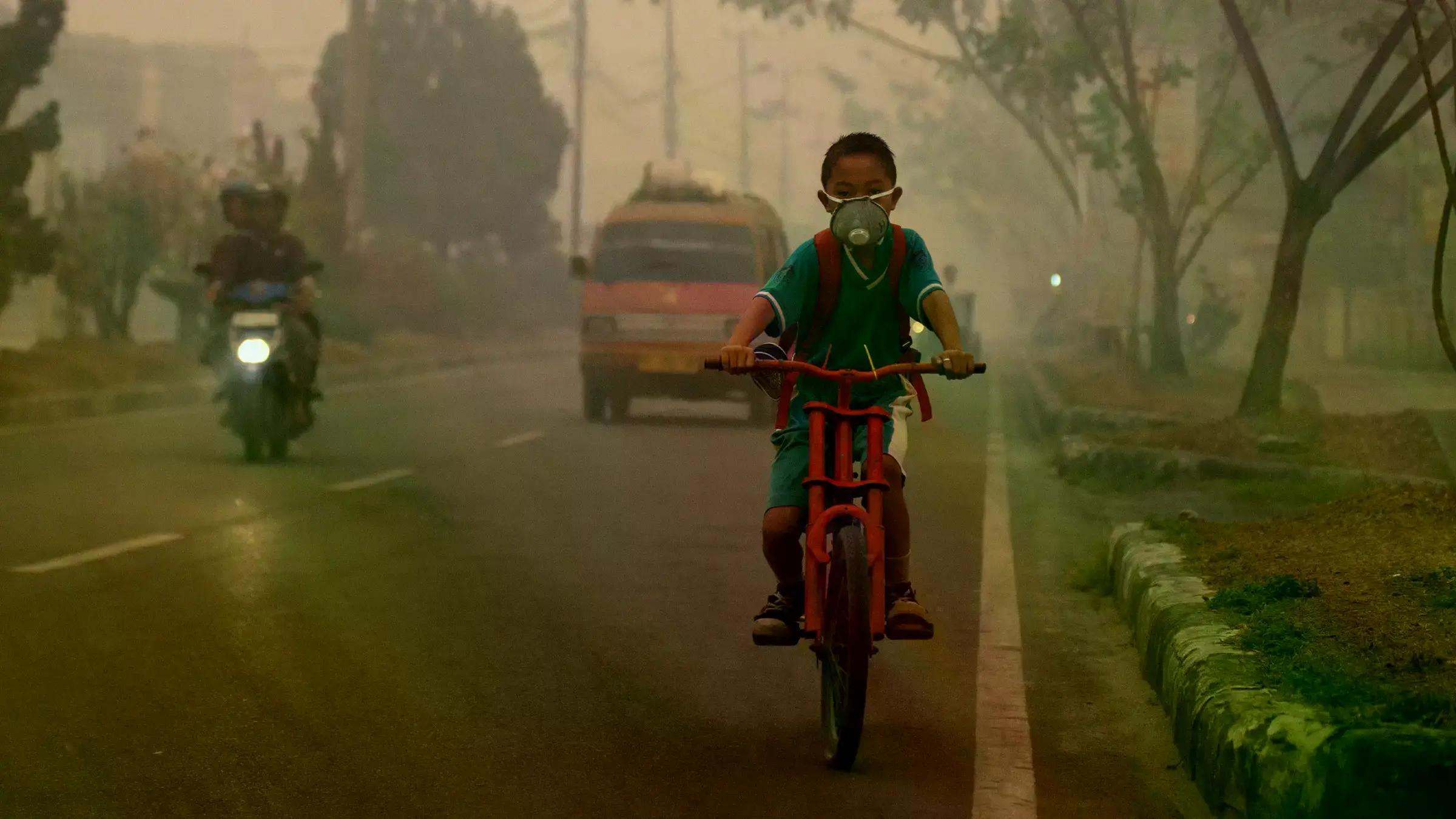 Un niño en bicicleta atraviesa una espesa niebla por incendios de turberas en Sumatra del Sur.